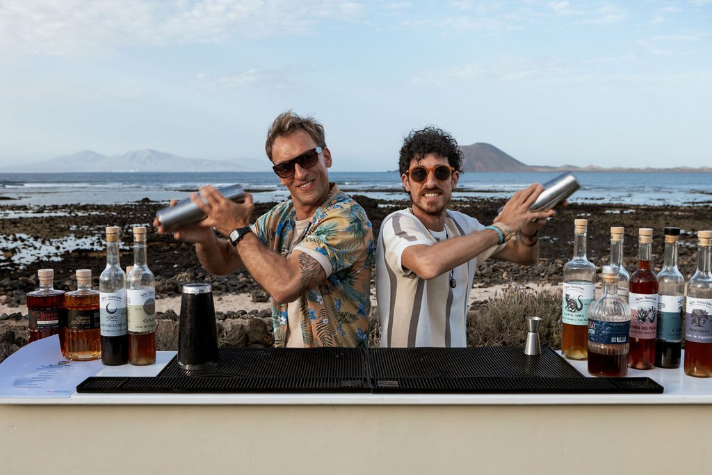 Bartenders de InFlow preparando cócteles en coctelera con el mar y el volcán de Lobos de fondo, en Fuerteventura