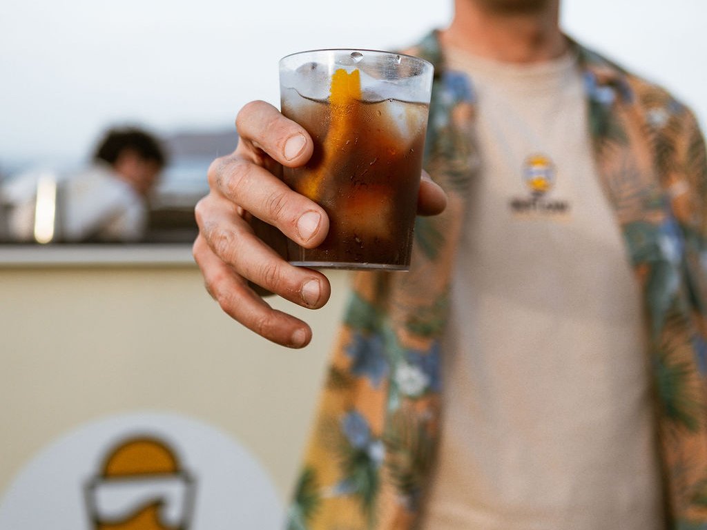 Copa recién servida por InFlow en la mano de un invitado, con el logotipo de la barra al fondo, durante un evento privado